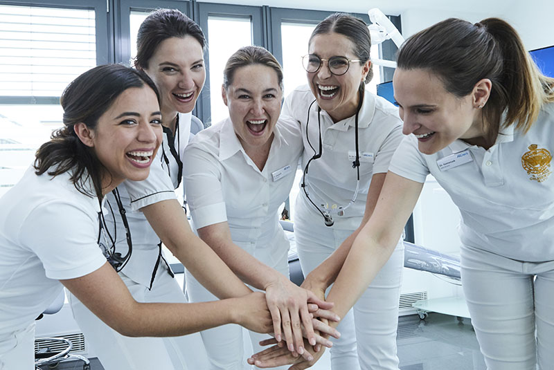 Fünf Zahnärztinnen stehen zusammen und haben Handflächen aufeinander gelegt